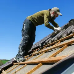 Pracownik naprawia dach dwuspadowy. Szacowany koszt dachu dwuspadowego 200m2 może być wysoki.