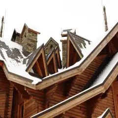 Drewniany dom z wieloma dachami i kominami, pokryty śniegiem. Widać tu architektoniczne detale, które mogą być odpowiedzią na pytanie: lukarna co to.