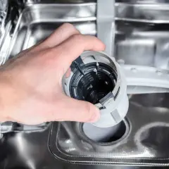 Ręka wyjmuje filtr zmywarki, który może być przyczyną, że zmywarka nie domywa naczyń.