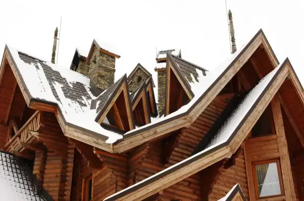 Drewniany dom z wieloma dachami i kominami, pokryty śniegiem. Widać tu architektoniczne detale, które mogą być odpowiedzią na pytanie: lukarna co to.