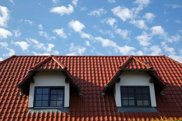 Dachówka ceramiczna w kolorze ceglastym pokrywa dach domu z dwoma lukarnami. Różne rodzaje dachówek tworzą harmonijną całość.