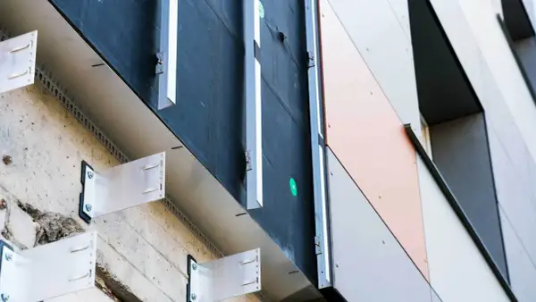 System mocowania elewacji wentylowanej z metalowymi wspornikami przytwierdzonymi do betonowej ściany, tworzący przestrzeń wentylacyjną.