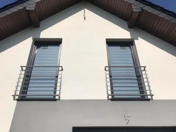Dwa nowoczesne portfenetry z metalowymi balustradami na białej elewacji domu.