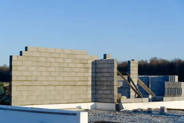 Budowa domu w toku. Wznoszona jest ściana nośna z bloczków betonowych, widoczne fundamenty i materiały budowlane.